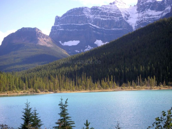 Turquoise lake in front of a snow-covered giant mountain in the Rocky Mountains